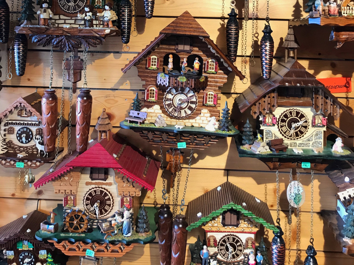 Wooden cuckoo clocks in different sizes and designs cover a shop display in Triberg im Schwarzwald, Germany. The clocks feature carved houses, painted figures, pendulums and decorative weights.