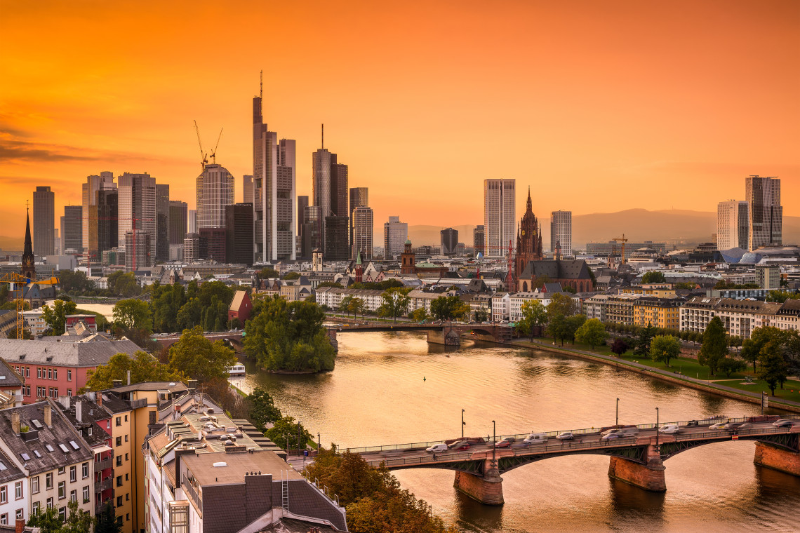 Frankfurt&rsquo;s modern skyline glowing at sunset above the Main River, with bridges and the historic city center in the foreground.