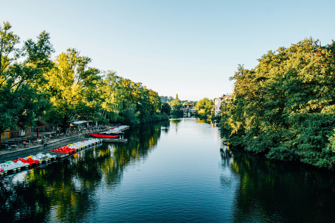 Calm tree-lined Lahn River in Marburg with small leisure boats moored along the waterfront.