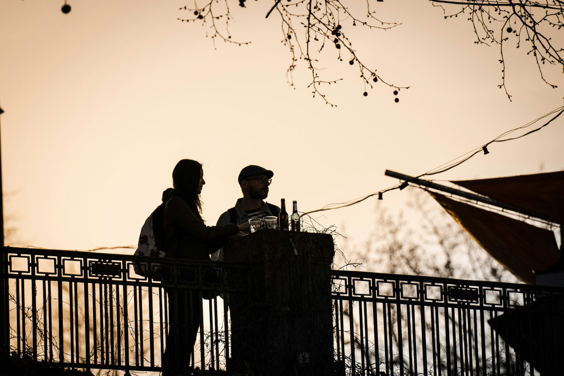 Two people enjoy drinks outdoors at sunset in a relaxed German beer garden setting.