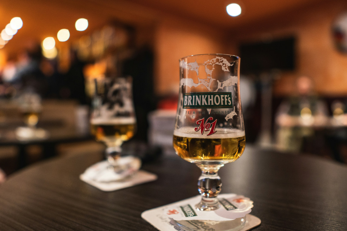 Close-up of a glass of Brinkhoff&rsquo;s No. 1 pilsner served on a table inside a traditional German bar.