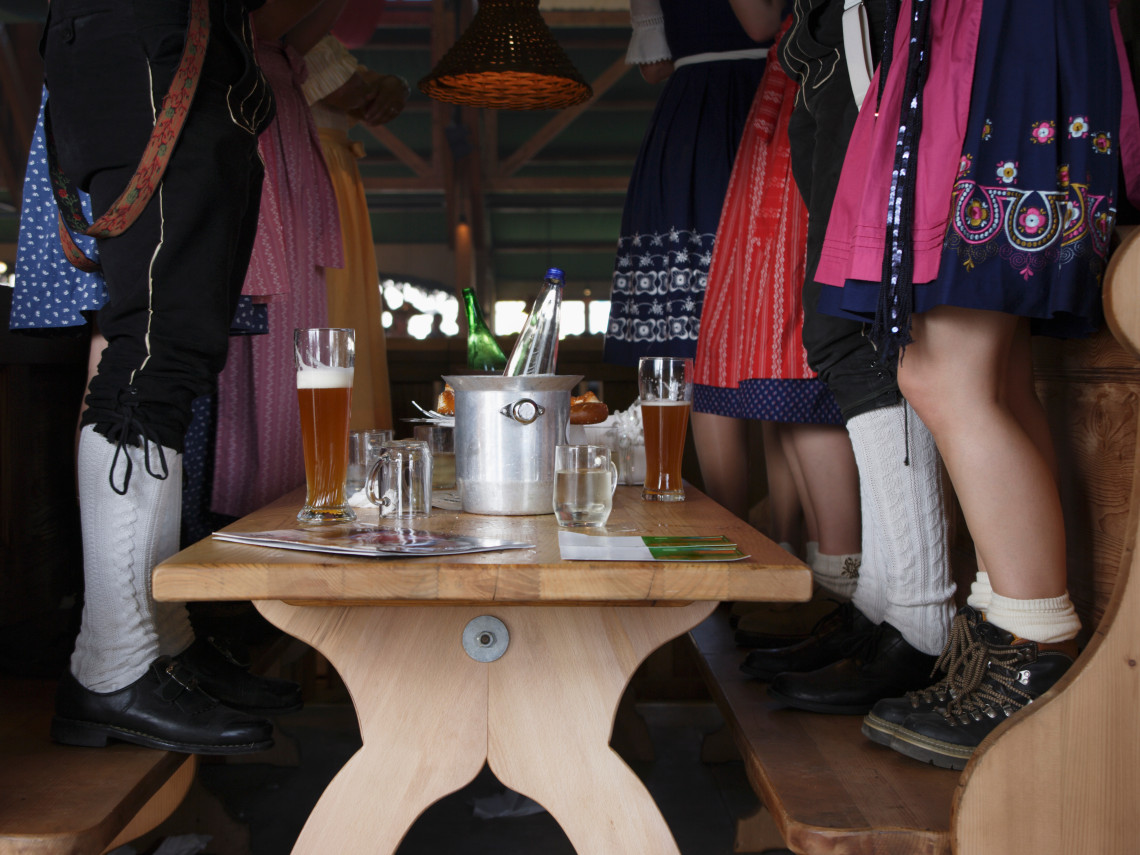 Guests wearing traditional Bavarian dirndls and lederhosen gather around a table with beer steins during Oktoberfest in Munich.