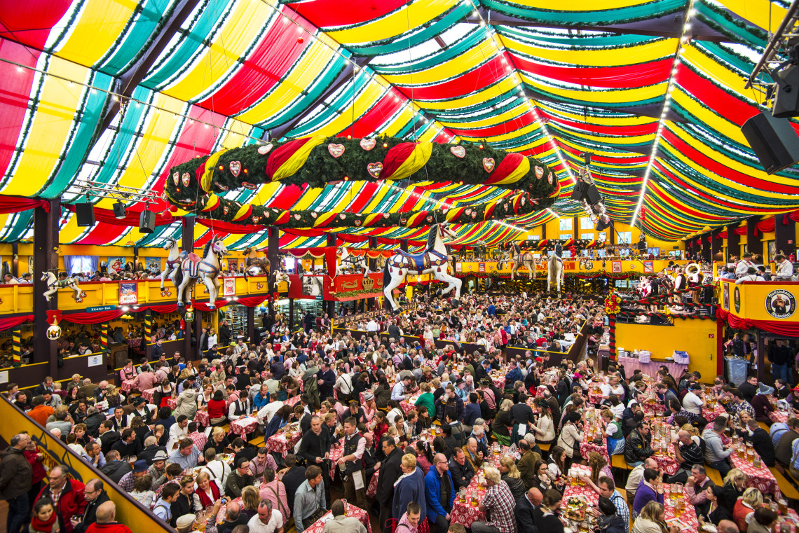 A packed Oktoberfest beer tent in Munich filled with festival visitors beneath colorful decorations and traditional Bavarian d&eacute;cor.