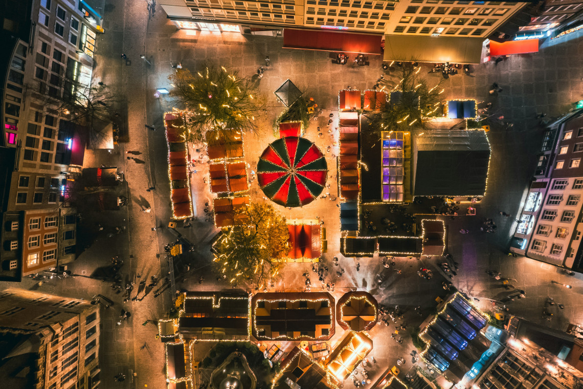 Aerial night view of Aachen Christmas Market in Aachen, Germany, showing illuminated wooden stalls, decorated Christmas trees and a red-and-green carousel in the historic city centre.