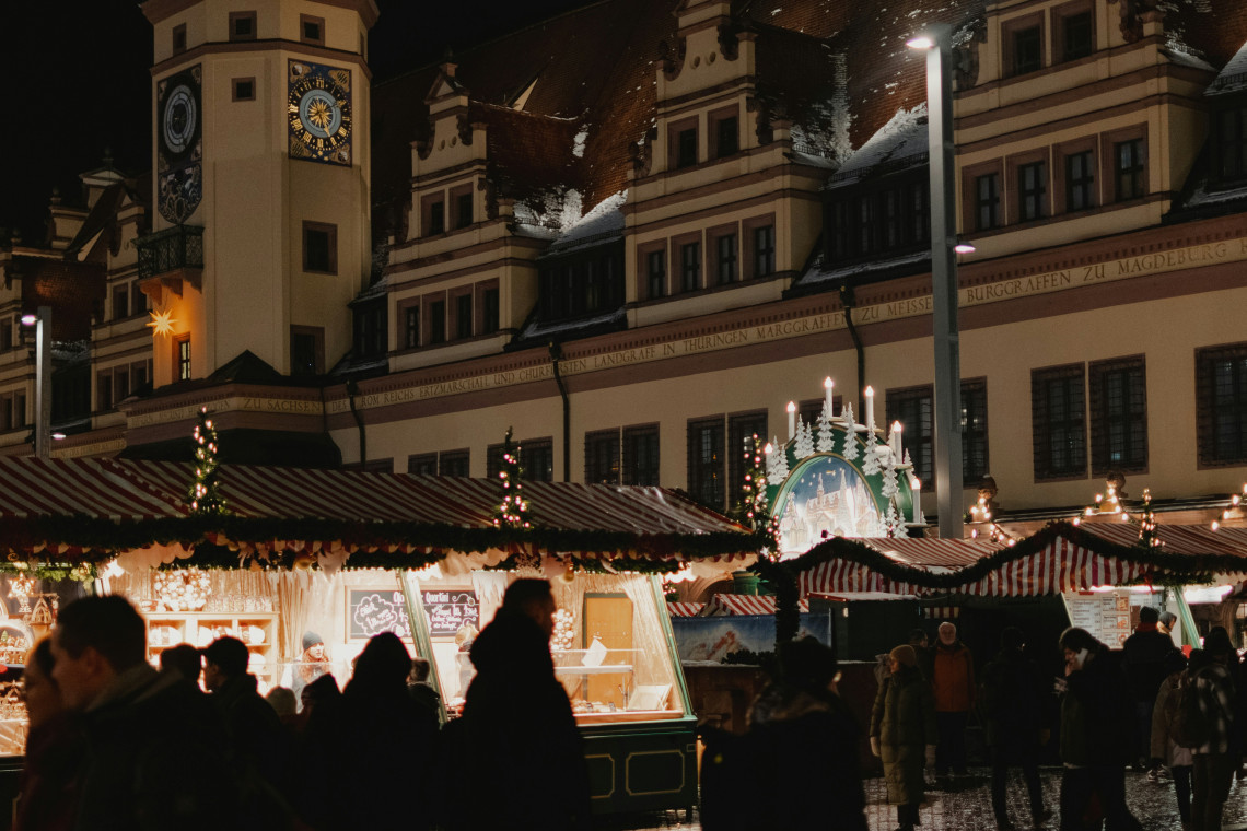 Evening view of Stuttgart Christmas Market in Stuttgart, Germany, with illuminated wooden stalls, snow-covered rooftops and a decorated Christmas tree surrounded by historic buildings in the city centre.