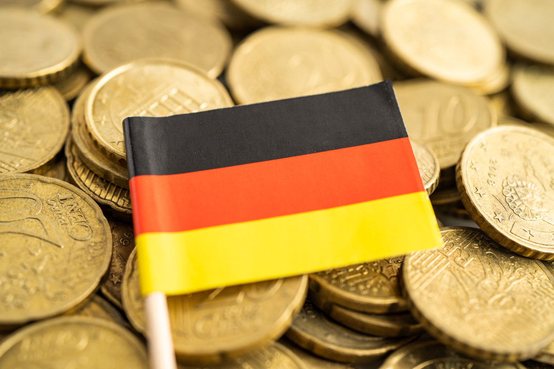 A small German flag rests on a pile of euro coins, representing currency and travel expenses in Germany.