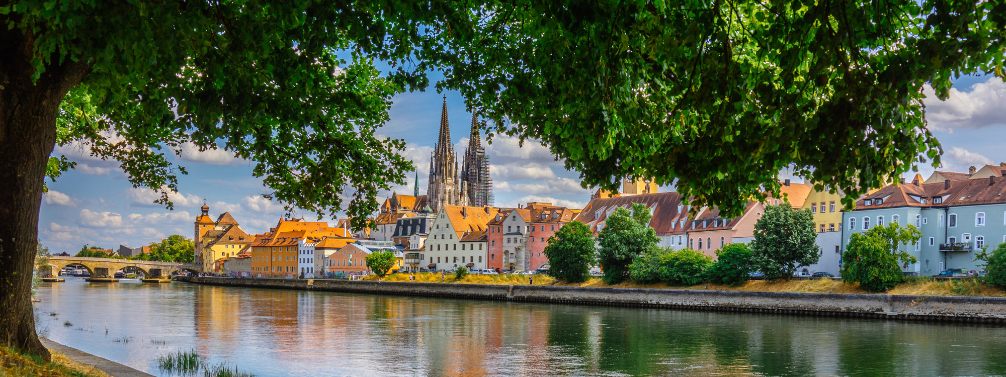 Colourful historic buildings and an arched stone bridge line the Pegnitz River in Nuremberg, Germany. The architecture and surrounding trees are reflected in the calm water.