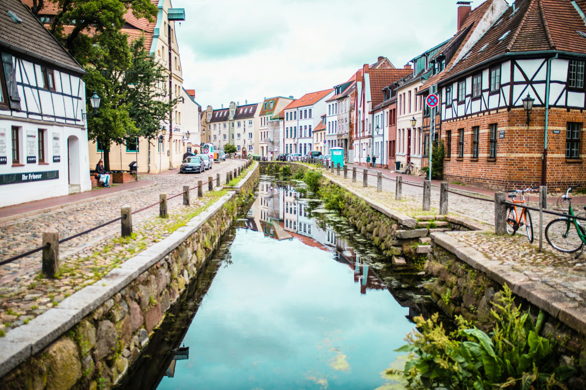 The Grube Canal passes between historic houses in Wismar, Germany. Cobblestone paths, bicycles and half-timbered architecture line the narrow Old Town waterway.