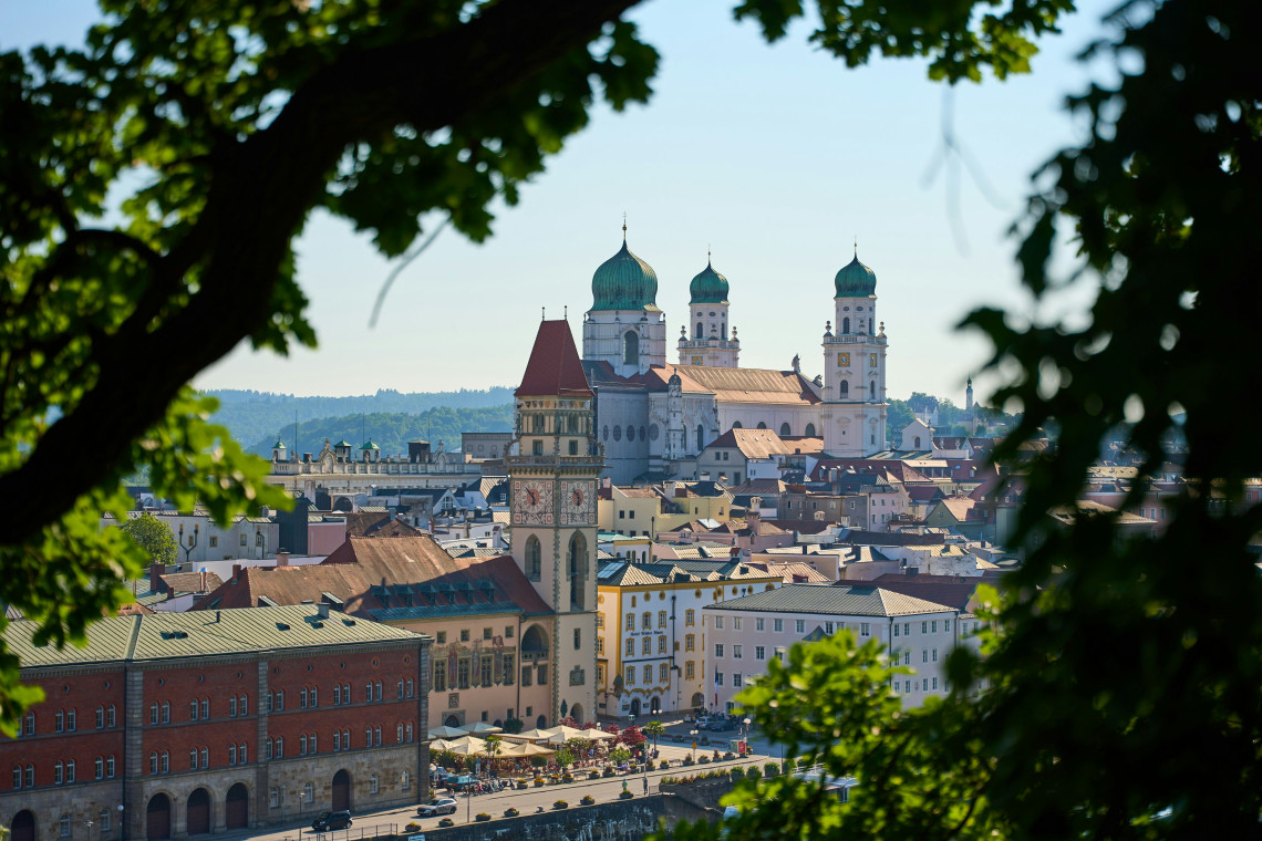 An elevated view overlooks Passau Old Town in Passau, Germany, with St Stephen&rsquo;s Cathedral rising above the city centre. Historic rooftops, church towers and public squares extend towards the surrounding hills.