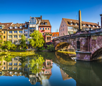 Regensburg Cathedral rises above the historic waterfront beside the Danube River in Regensburg, Germany. Colourful Old Town buildings and the Stone Bridge extend along the riverbank.