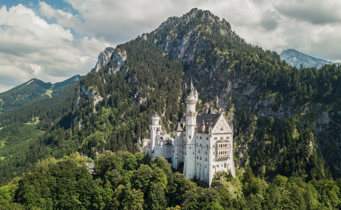 Neuschwanstein Castle stands on a forested hillside near Schwangau, Germany, surrounded by the rocky peaks and wooded slopes of the Bavarian Alps.