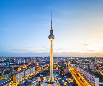 The Berlin TV Tower rises above central Berlin, Germany, as city streets and buildings begin to illuminate at sunset.