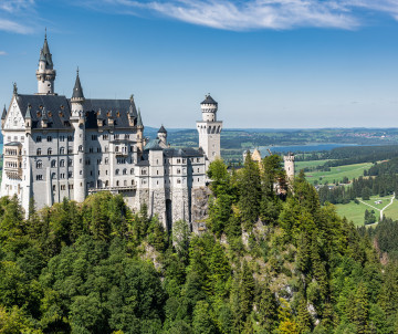 Neuschwanstein Castle rises from a forested ridge near Schwangau, Germany, overlooking the lakes, fields and foothills of the Bavarian Alps.