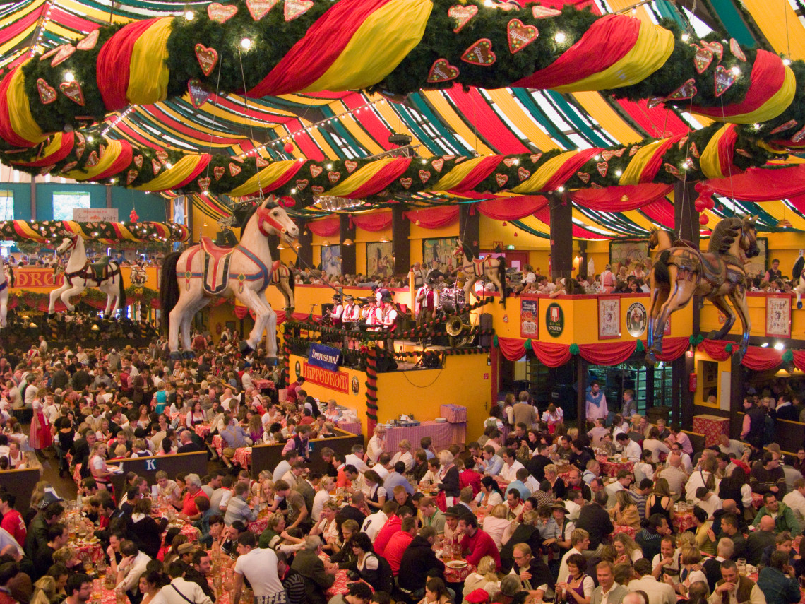 Festivalgoers fill a decorated beer tent at Oktoberfest in Munich, Germany. Colourful fabric, hanging horses and Bavarian decorations extend above the crowded communal tables.