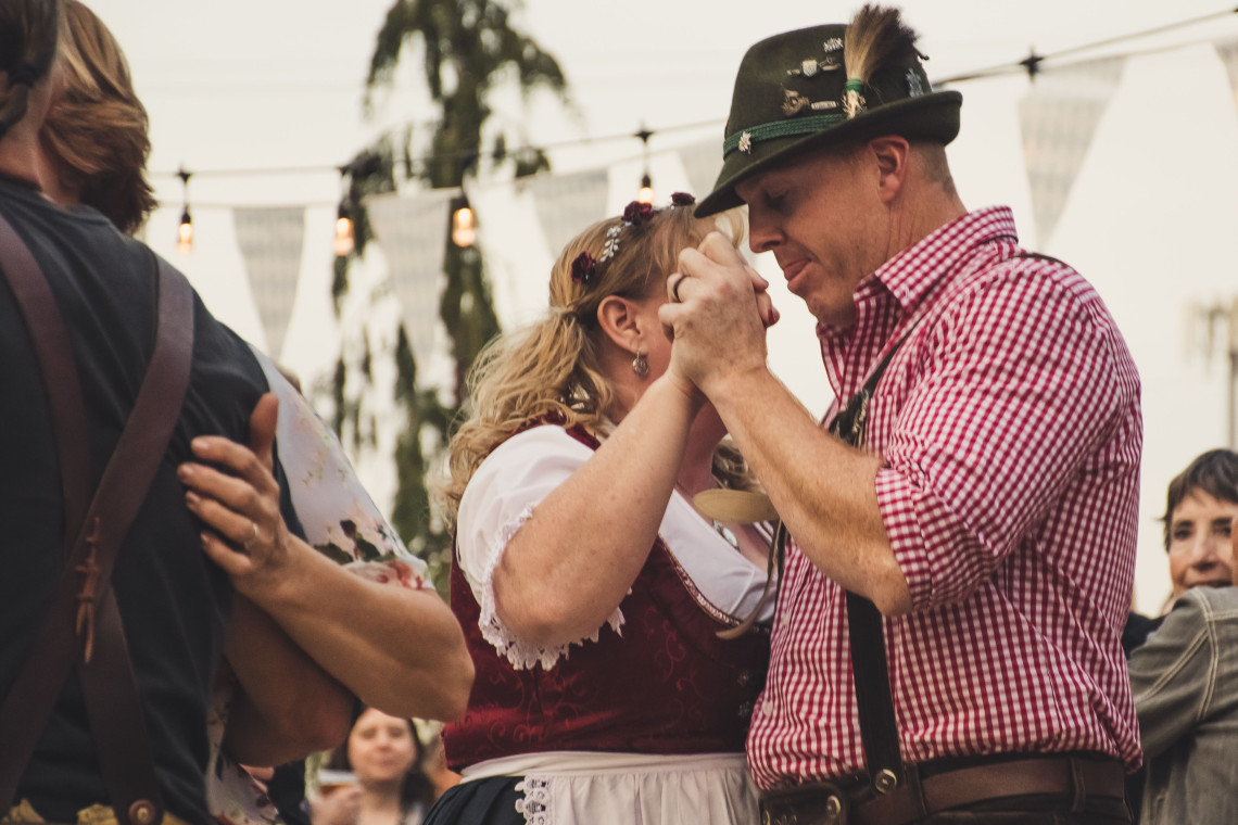 A couple wearing traditional Bavarian clothing dances together during a festival in Munich, Germany. The man wears lederhosen and an Alpine hat, while the woman wears a dirndl.