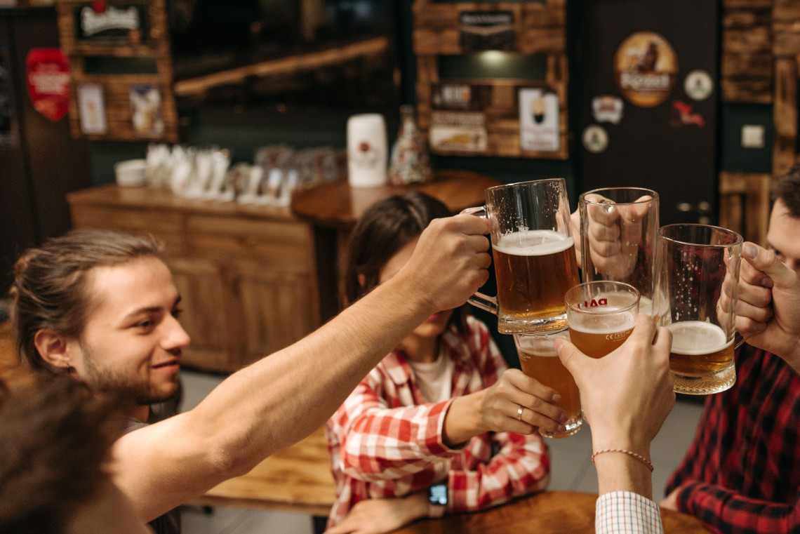 A group of friends raises glass beer mugs for a toast inside a traditional beer hall in Munich, Germany. Wooden furnishings and Bavarian-style d&eacute;cor frame the gathering.