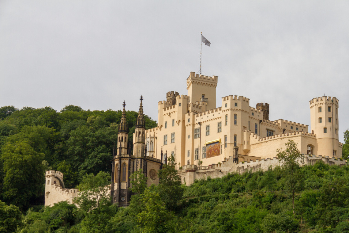 Stolzenfels Castle rises above a wooded hillside in Koblenz, Germany. The pale palace features crenellated towers, Gothic architectural details and an adjoining chapel.