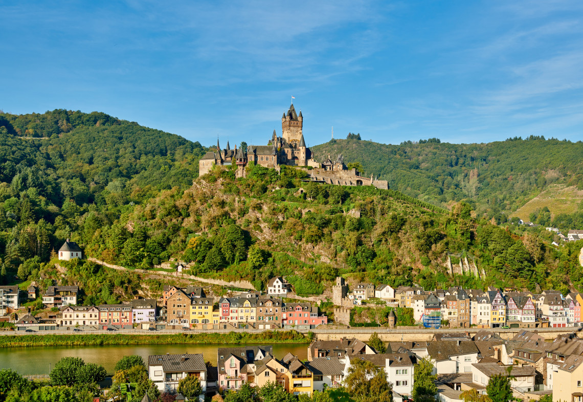 Reichsburg Cochem stands on a vineyard-covered hill above Cochem, Germany. Colourful riverside buildings and the Moselle River extend below the historic castle.