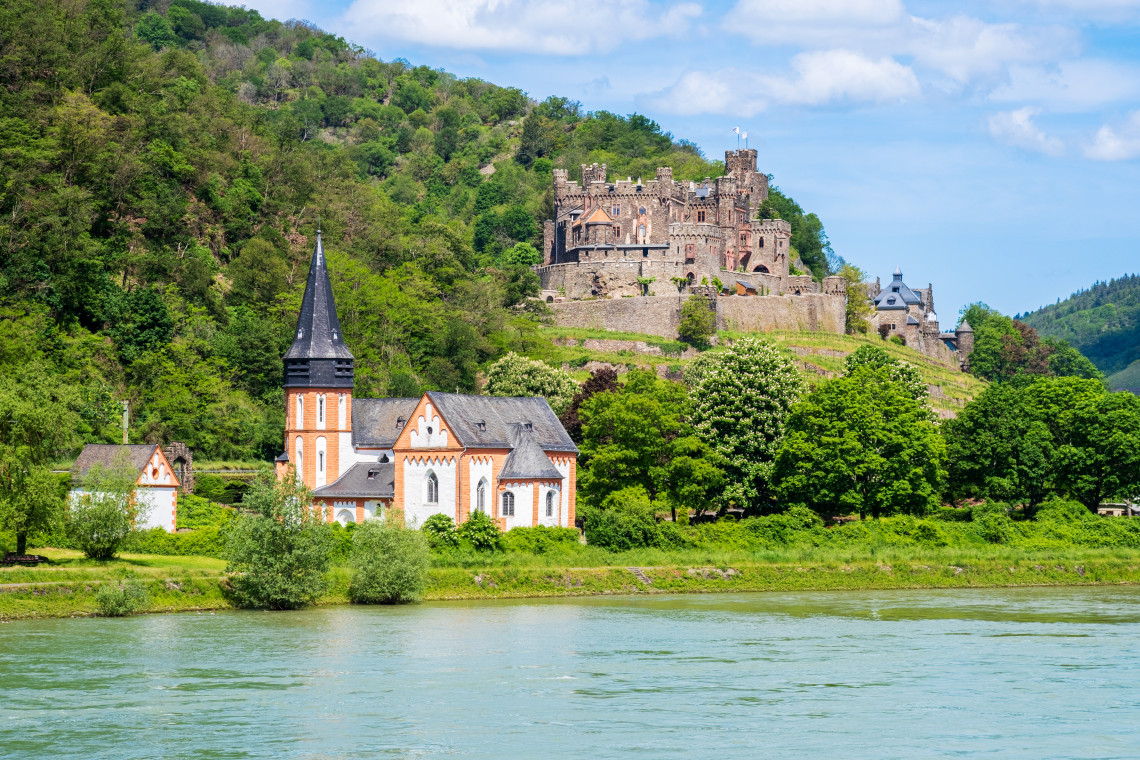 Reichenstein Castle rising above St. Clement&rsquo;s Chapel on a forested hillside beside the Rhine River in Trechtingshausen, Germany.