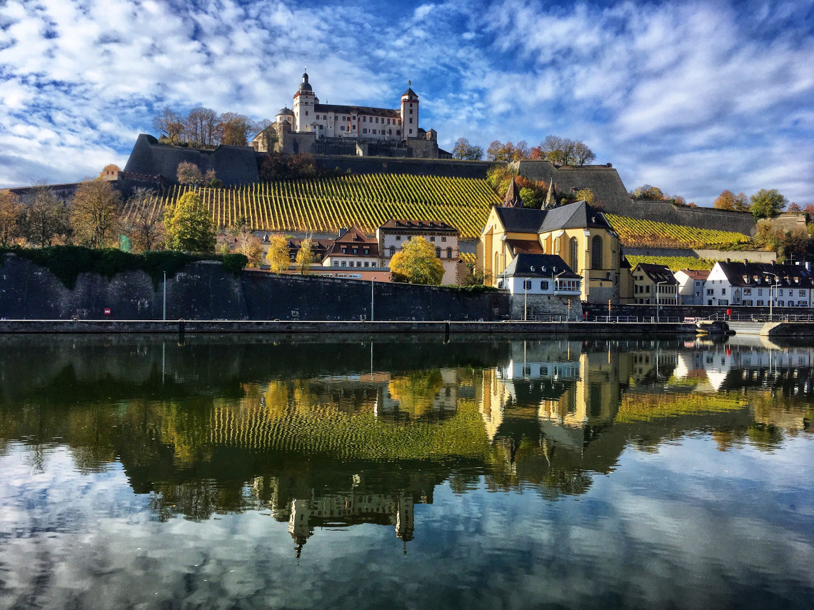 Marienberg Fortress rising above vineyard-covered slopes in W&uuml;rzburg, reflected in the calm waters of the Main River.