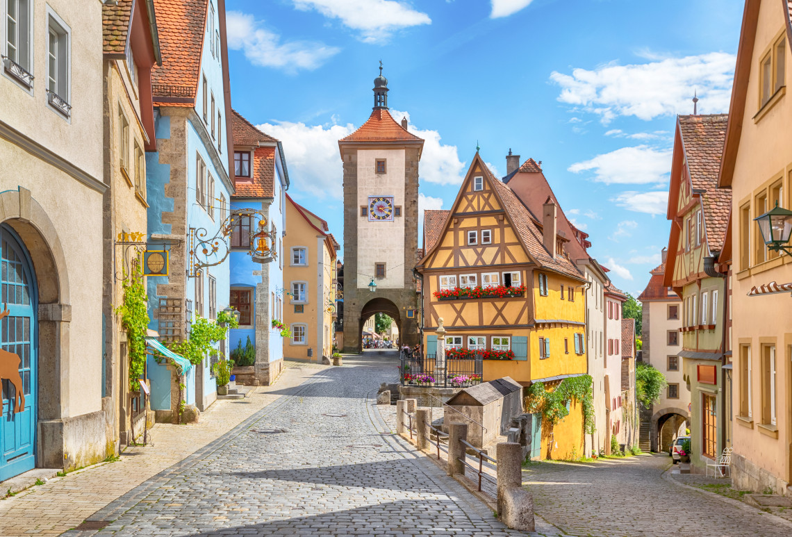 Colorful medieval houses and a historic gateway line a cobblestone street in the preserved old town of Rothenburg ob der Tauber.