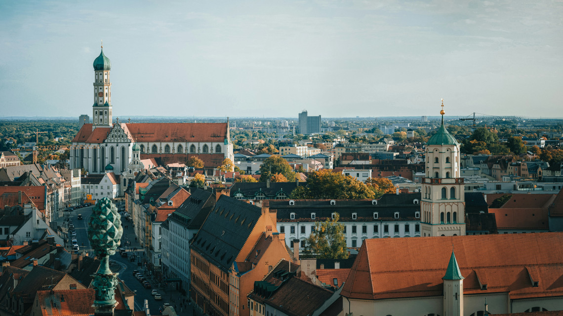 Elevated view across Augsburg&rsquo;s historic center, with church towers, red-tiled rooftops and urban landmarks extending across the Bavarian city.