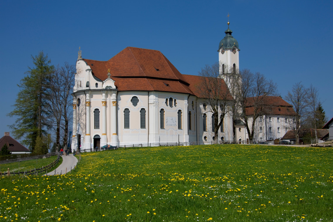 The white Rococo Wieskirche stands beside a green meadow near Steingaden, surrounded by the rural landscape of southern Bavaria.