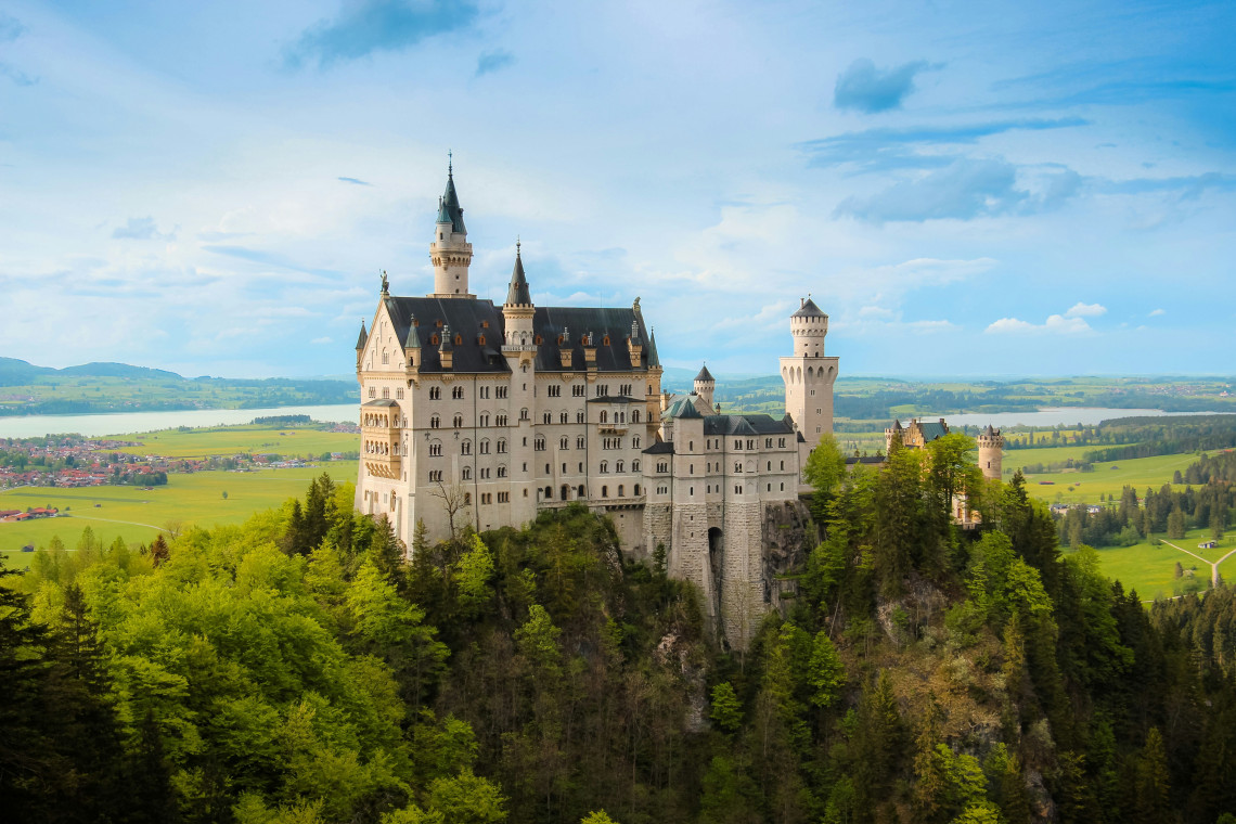Neuschwanstein Castle rises above a forested rocky hill near Schwangau, surrounded by the rolling landscape of the Bavarian Alps.
