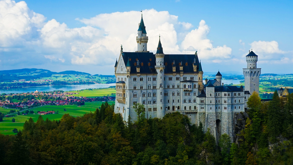 Neuschwanstein Castle stands on a forested hillside near Schwangau, Germany, overlooking the fields, villages and lakes of the Bavarian countryside.
