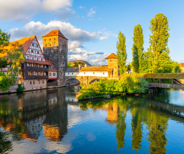 The half-timbered Weinstadel and adjoining Henkersteg stand beside the Pegnitz River in Nuremberg, Germany. Historic buildings and autumn trees reflect in the calm water.