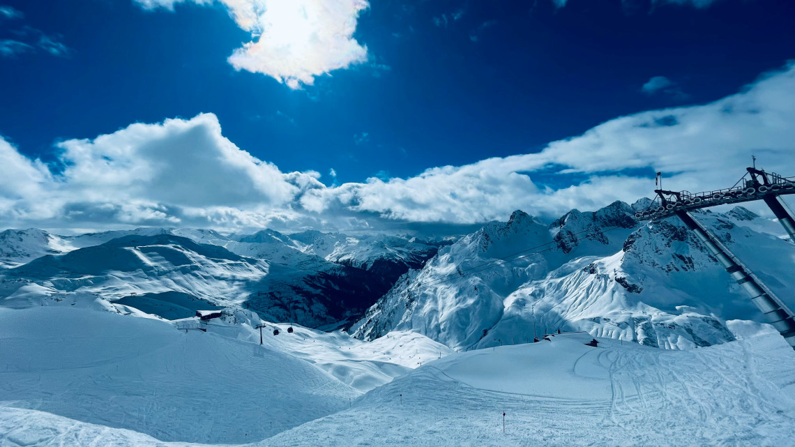 High-altitude ski slopes overlook a rugged Alpine valley at St Anton am Arlberg in Austria. Snow-covered peaks, lift infrastructure and marked ski routes extend across the mountain terrain.