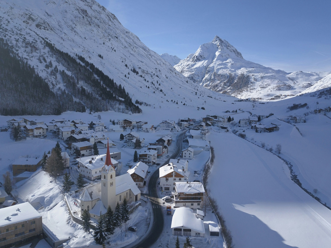 The village of Ischgl, Austria, lies beneath snow-covered mountains in the Paznaun Valley. Alpine houses, a church tower and winter roads fill the compact ski resort.