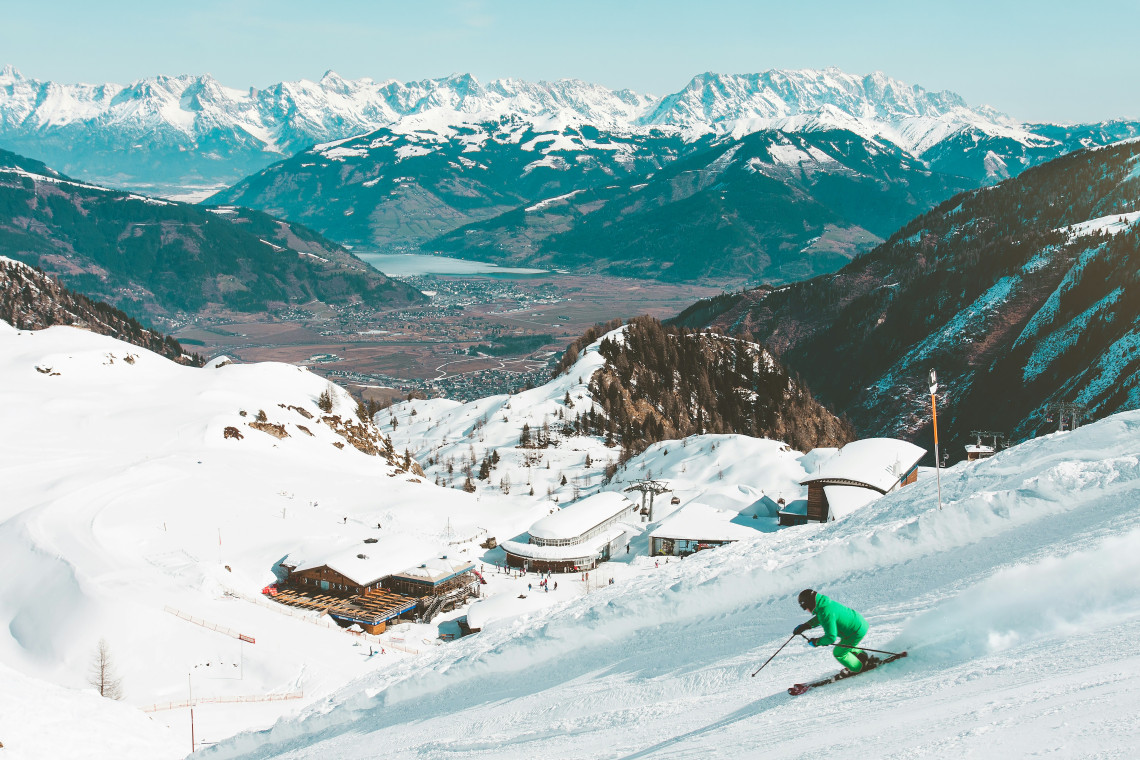A skier descends the snow-covered slopes of the Kitzsteinhorn ski area near Kaprun, Austria. Mountain facilities overlook the Zell am See valley and surrounding Alpine ranges.
