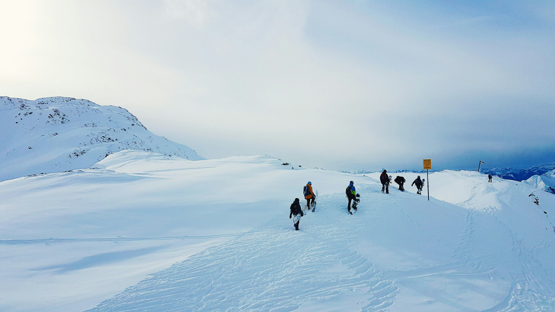 A group of hikers follows a marked winter trail across a snow-covered plateau near Obergurgl, Austria. Open slopes and distant Alpine ridges surround the guided route.