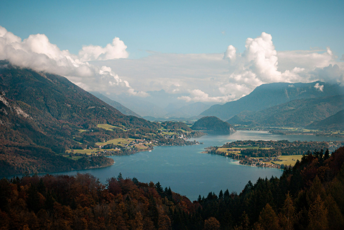 Elevated view of Lake Wolfgang in Austria&rsquo;s Salzkammergut region, surrounded by forested mountains, rural villages and farmland. The lake curves through the broad Alpine valley beneath layered clouds.