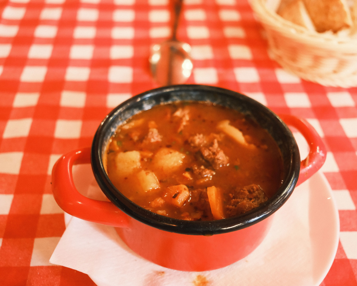 A bowl of Austrian goulash served in Vienna, Austria, with tender beef, vegetables and paprika-rich sauce. The hot stew is presented in a red enamel bowl beside bread.