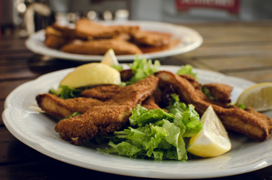 Traditional Austrian Backhendl served in Vienna, Austria, with breaded fried chicken pieces, green salad and lemon wedges. A second plate appears softly blurred in the background.