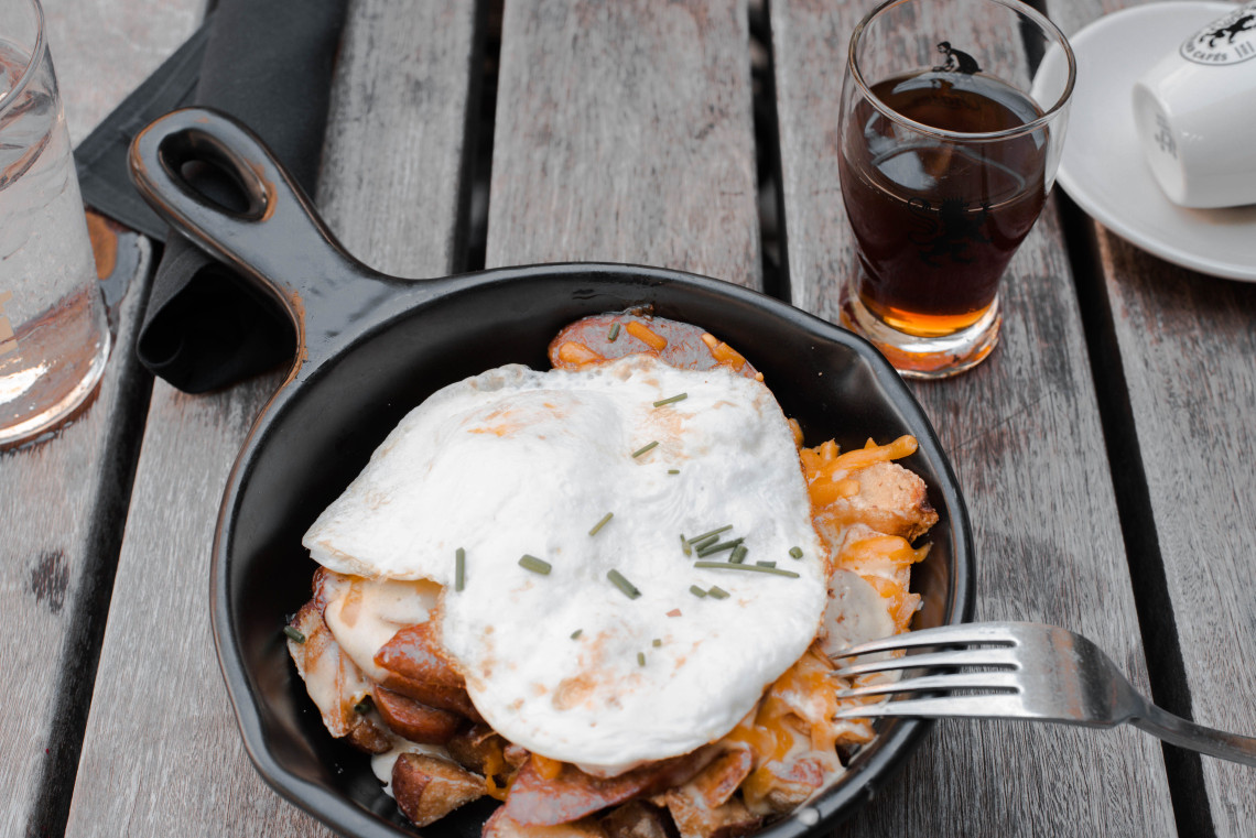 Tiroler Gr&ouml;stl served in Tyrol, Austria, with pan-fried potatoes, onions and meat beneath two fried eggs. The Alpine dish is presented in a black skillet on a wooden table.