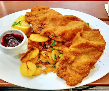 Traditional Wiener Schnitzel served in Vienna, Austria, with golden breaded veal cutlets, pan-fried potatoes, lemon and a small portion of cranberry sauce.