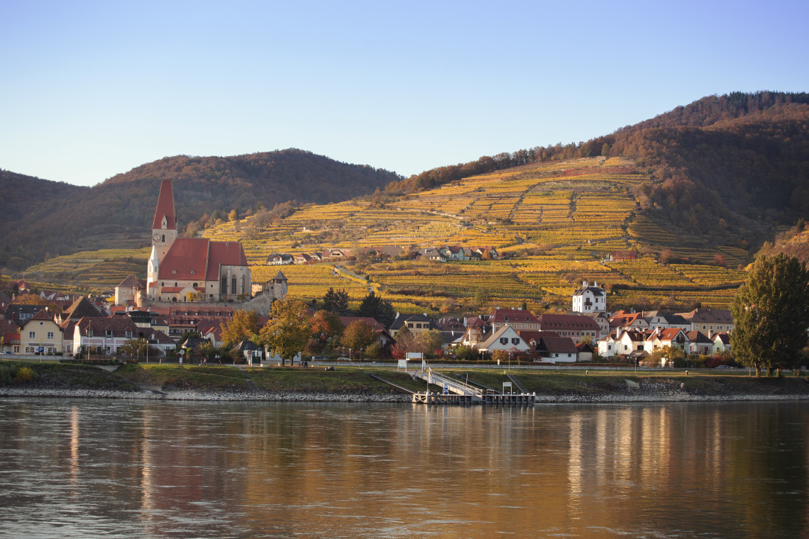 Spitz an der Donau stands beside the Danube River in Austria&rsquo;s Wachau Valley, with its church rising above red-roofed houses. Terraced vineyards cover the surrounding hills in autumn colours.