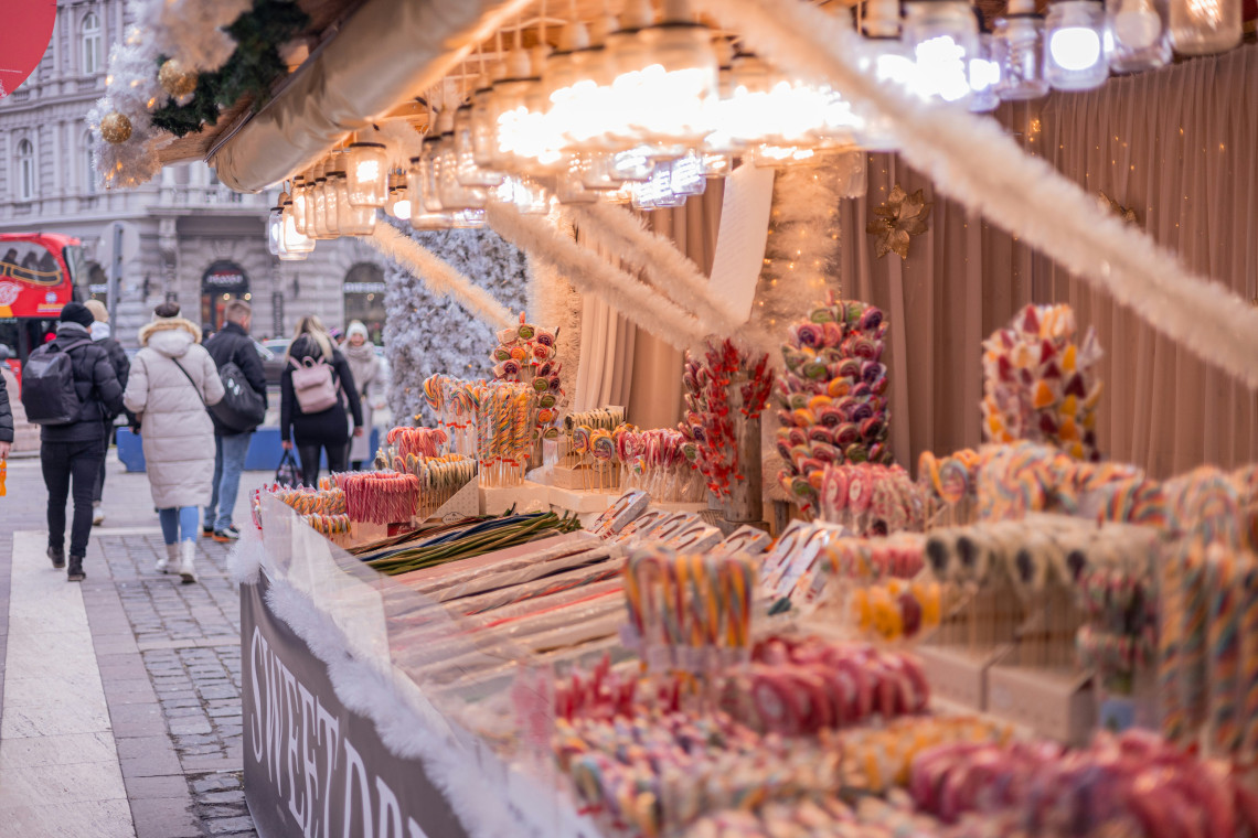A Christmas market stall in Budapest, Hungary, displays colourful candy canes, lollipops and other seasonal sweets beneath warm lights. Winter visitors walk past the decorated stand in the city centre.