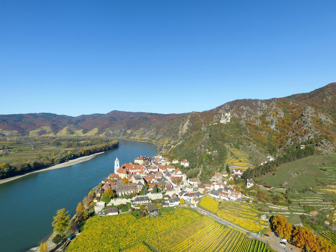 Aerial view of D&uuml;rnstein beside the Danube River in Austria&rsquo;s Wachau Valley. The riverside village is surrounded by terraced vineyards, autumn hills and the ruins of D&uuml;rnstein Castle.
