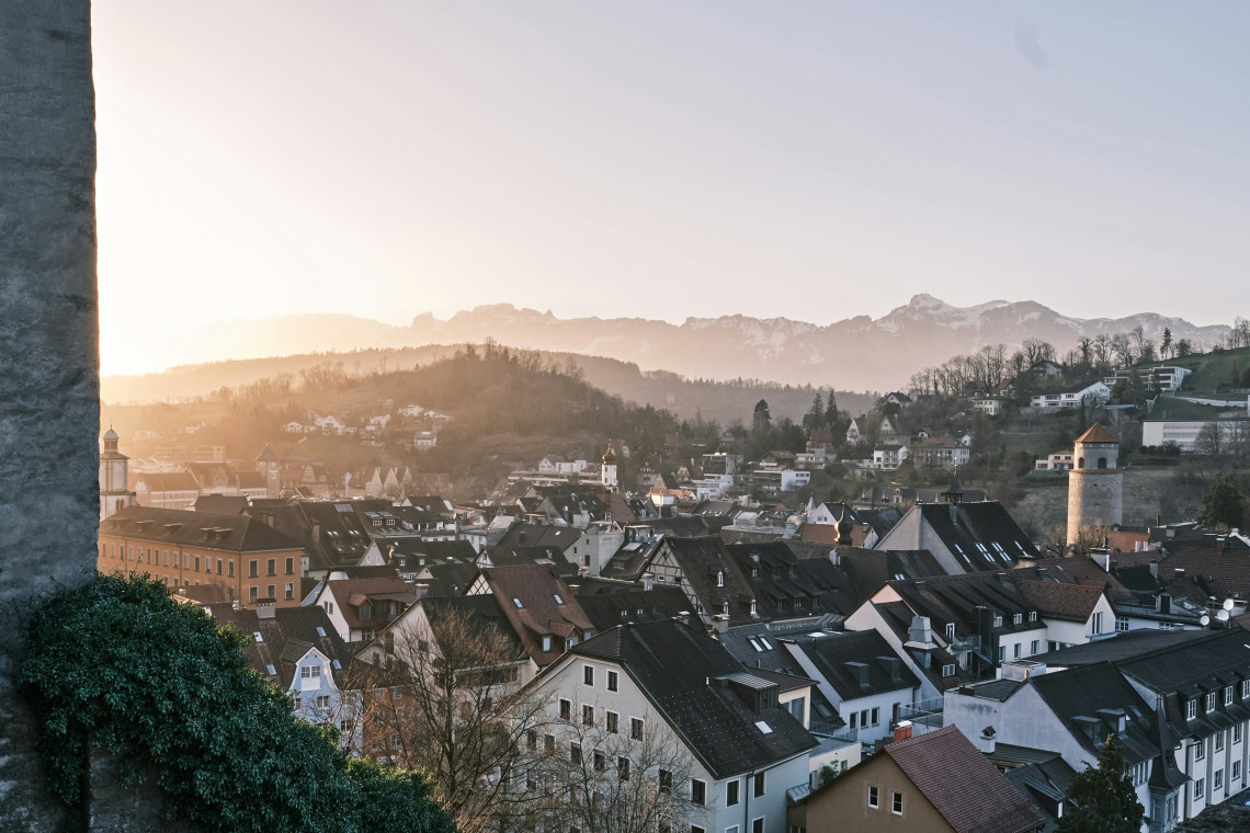 Elevated view across the historic rooftops and medieval towers of Feldkirch, Austria. The compact old town is surrounded by wooded hills and mountain ridges in Vorarlberg.