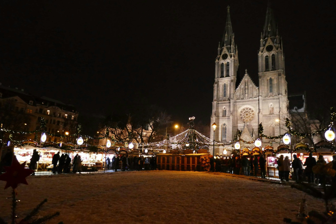 Christmas market stalls and strings of festive lights fill N&aacute;měst&iacute; M&iacute;ru in Prague, Czech Republic. The twin Gothic towers of St Ludmila Church rise behind the snow-covered square at night.
