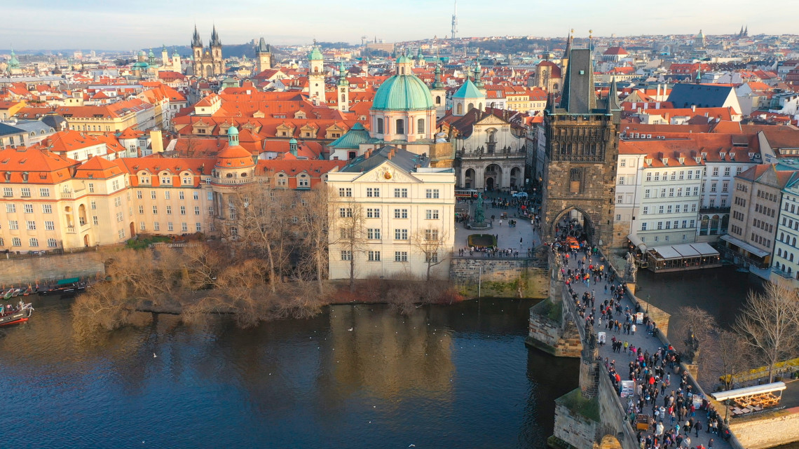 Elevated view of Charles Bridge crossing the Vltava River toward Prague&rsquo;s Old Town in the Czech Republic. The historic bridge towers, red rooftops and church domes extend across the cityscape.