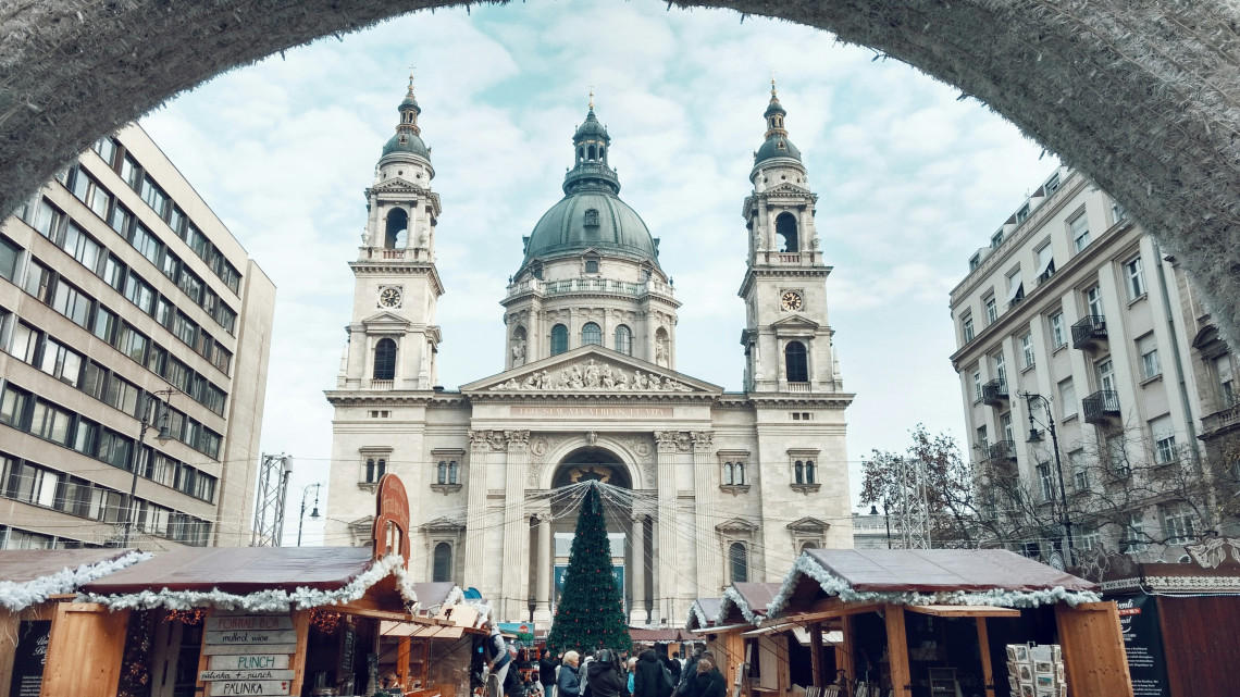 Wooden Christmas market stalls and a decorated tree stand in front of St Stephen&rsquo;s Basilica in Budapest, Hungary. The basilica&rsquo;s domed fa&ccedil;ade and twin bell towers rise above visitors in the city centre.