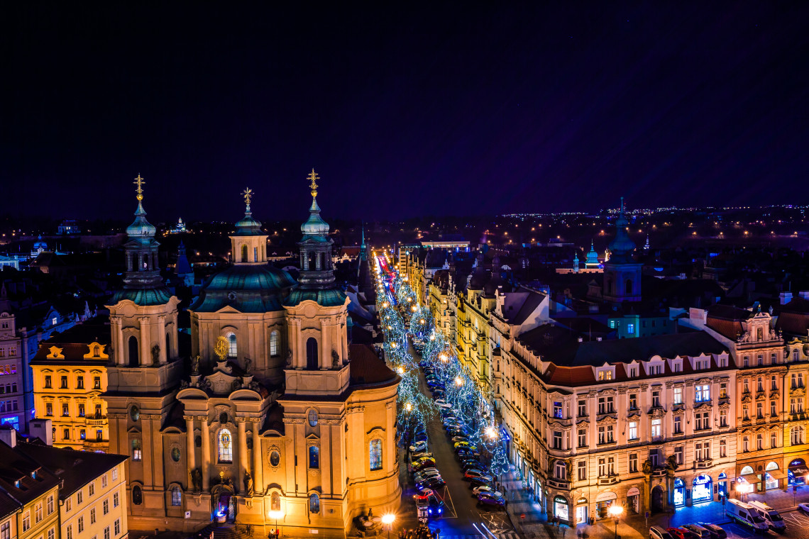 Night view of St Nicholas Church and Pař&iacute;žsk&aacute; Street in Prague, Czech Republic, with illuminated buildings and rows of seasonal lights. The decorated avenue stretches through the historic Old Town.
