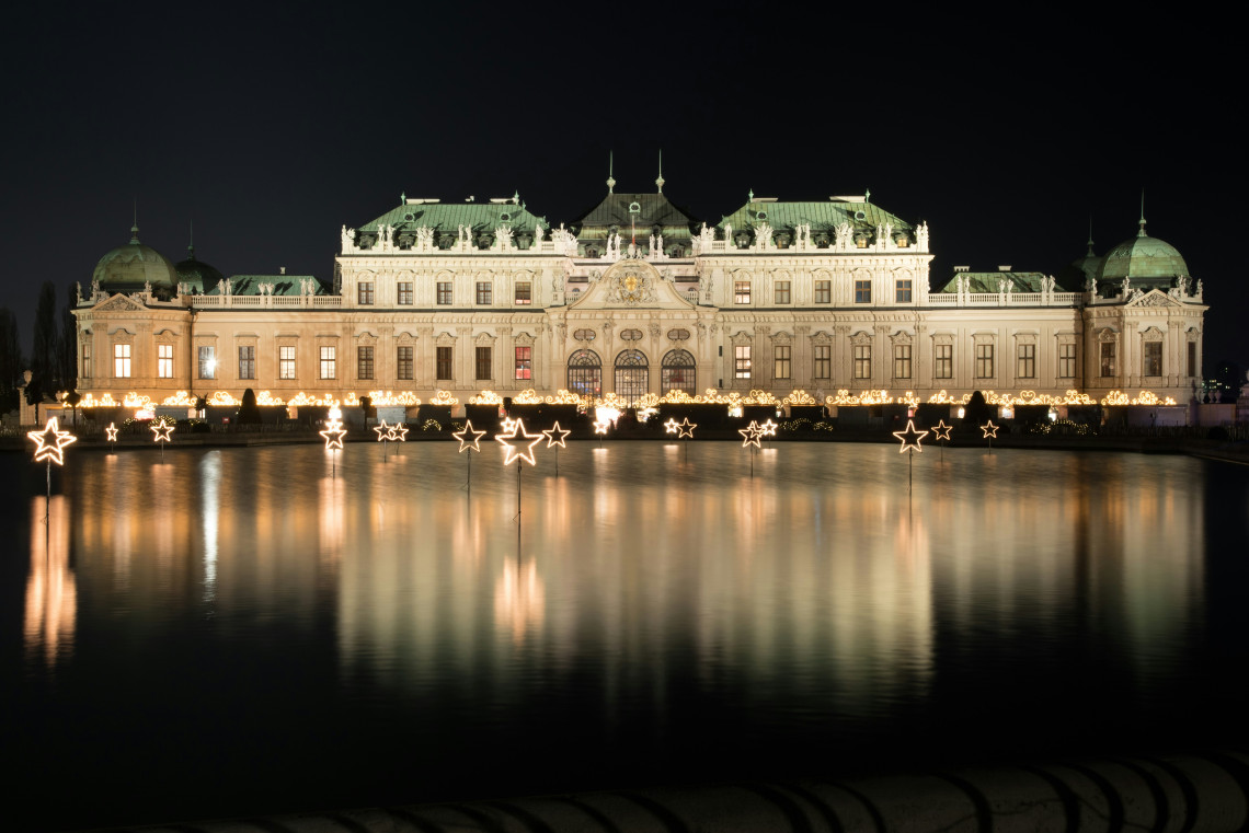 Upper Belvedere Palace in Vienna, Austria, illuminated at night and reflected in the large ornamental pond. Star-shaped seasonal lights line the water in front of the Baroque palace.