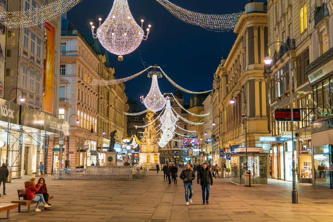 Large chandelier-shaped Christmas lights hang above the Graben pedestrian street in central Vienna, Austria. Historic buildings, shops and evening pedestrians line the decorated city-centre avenue.