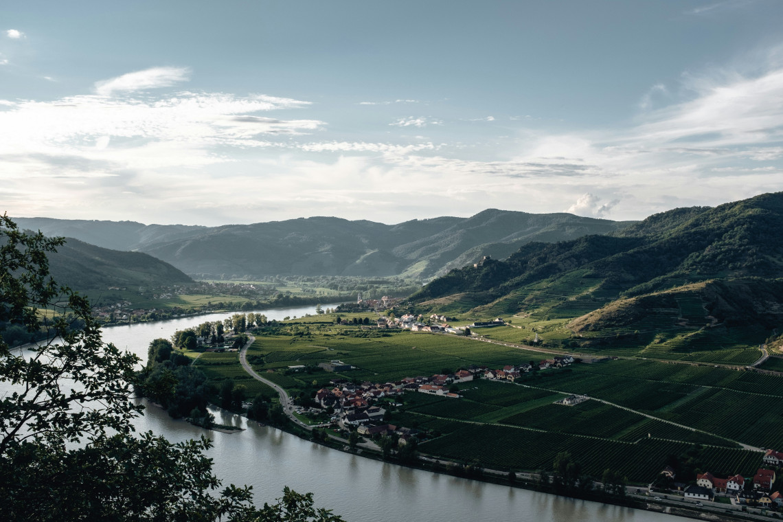 The Danube River curves through the Wachau Valley in Lower Austria, Austria, between vineyard-covered hills and small riverside villages. Roads, cultivated fields and wooded slopes extend across the valley.